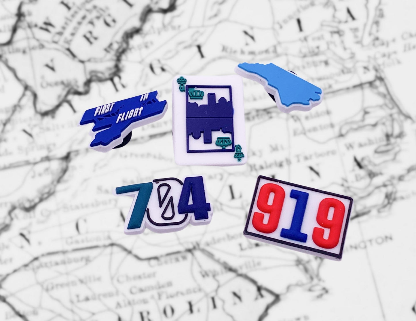 Malcontents North Carolina Croc Charms/Jibbitz pack: Queen City Card, North Carolina State, First in Flight, 919, and 704 in front of North Carolina map