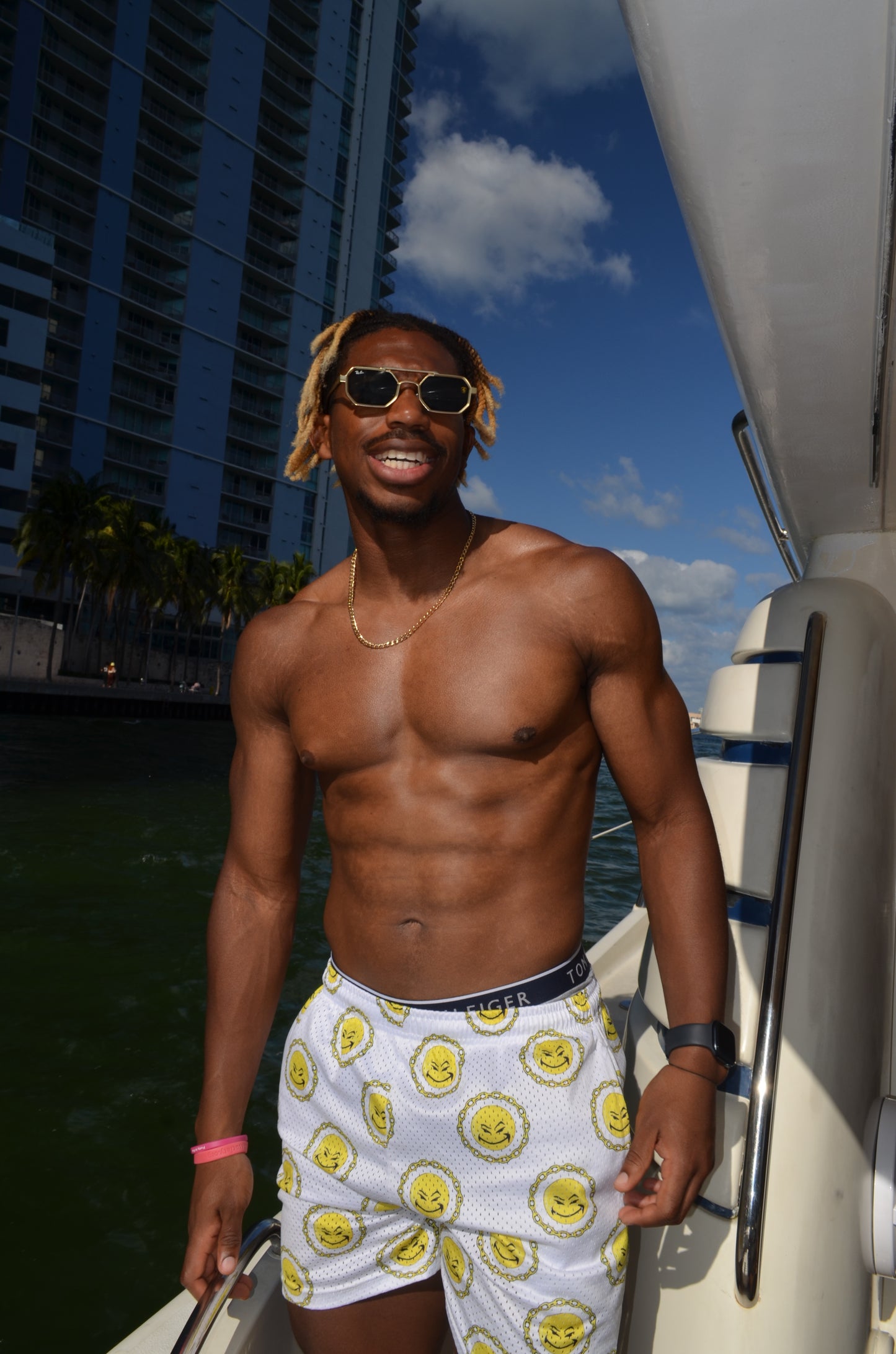 An image of a shirtless man wearing white shorts with repeated patter and sunglasses