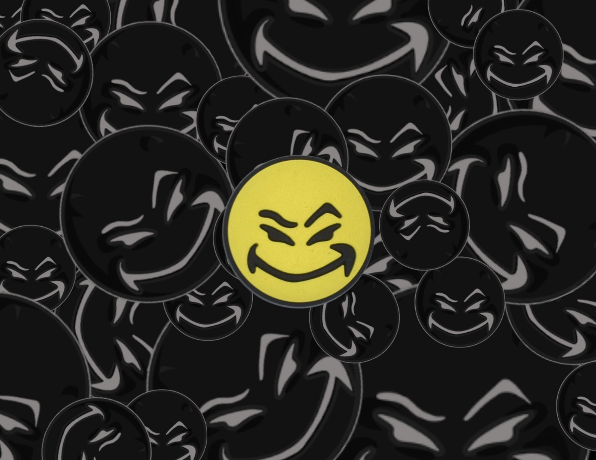 Malcontents Croc Charm/Jibbitz shows smiley logo with yellow face and mischievous smile in front of black smilies background.