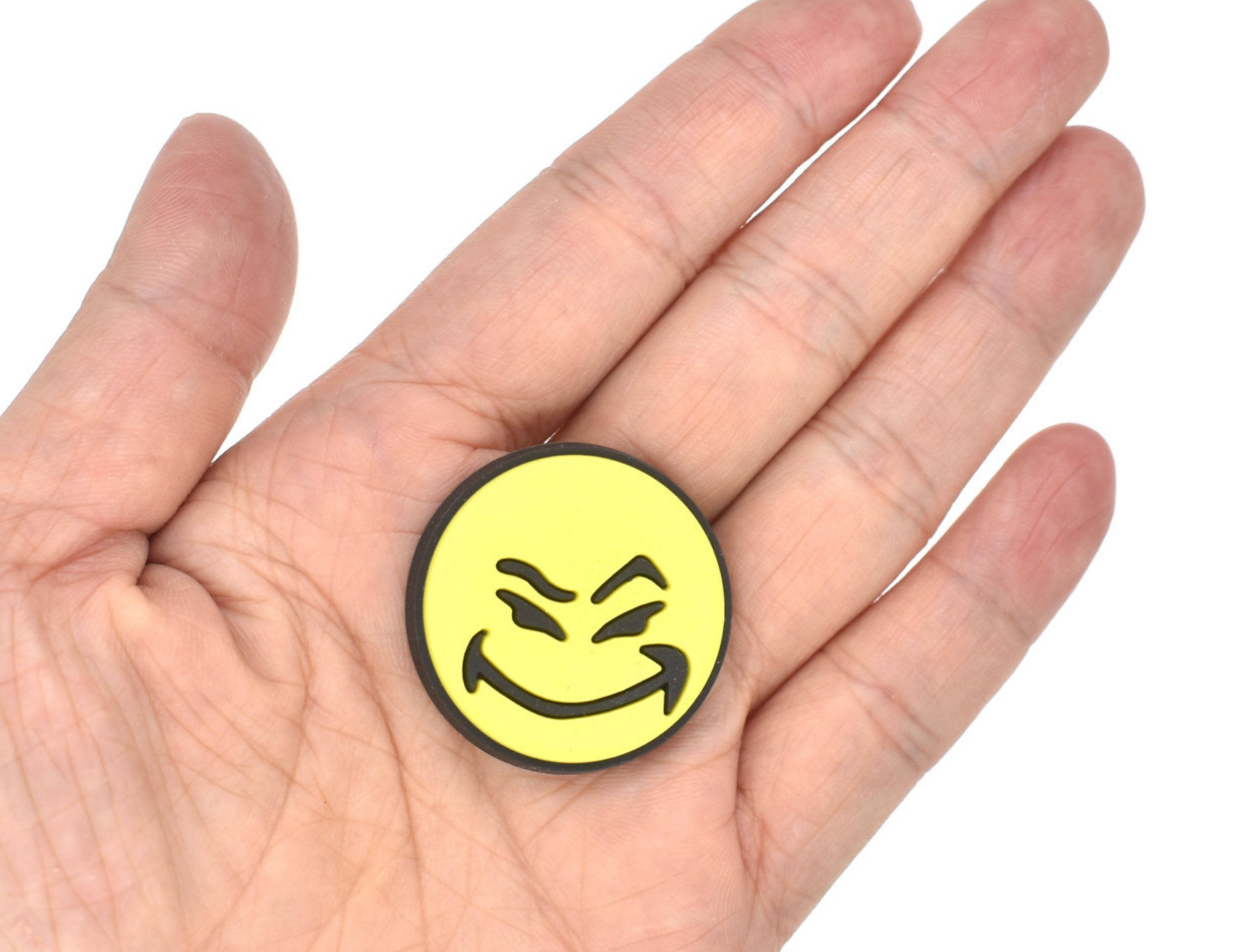 Malcontents Croc Charm/Jibbitz shows smiley logo with yellow face and mischievous smile on the palm of a hand