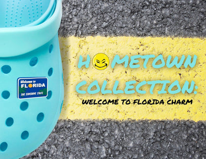 Malcontents Welcome to Florida Croc Charm/Jibbitz shows the blue "Welcome to Florida" sign with green palm trees, a yellow sun for the "O", and "The Sunshine State" in white letters on Blue crocs on the street